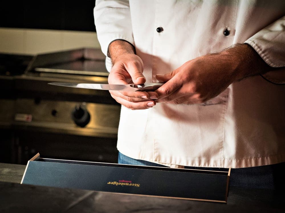 Hands holding a kitchen knife over a preparation board