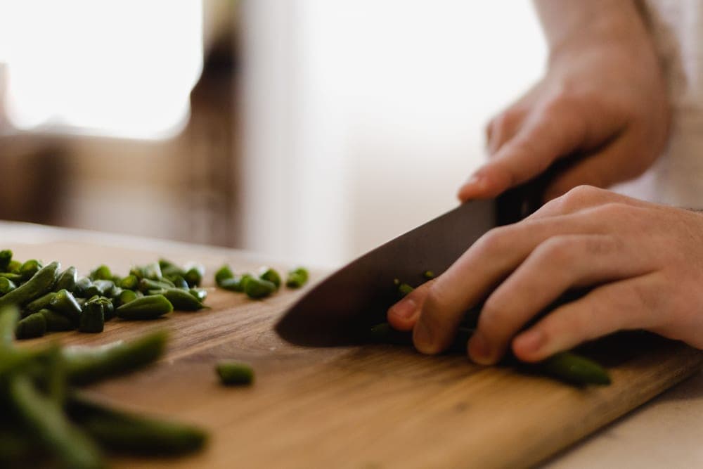 A thin-bladed Japanese chef's knife slicing vegetables on a wooden board