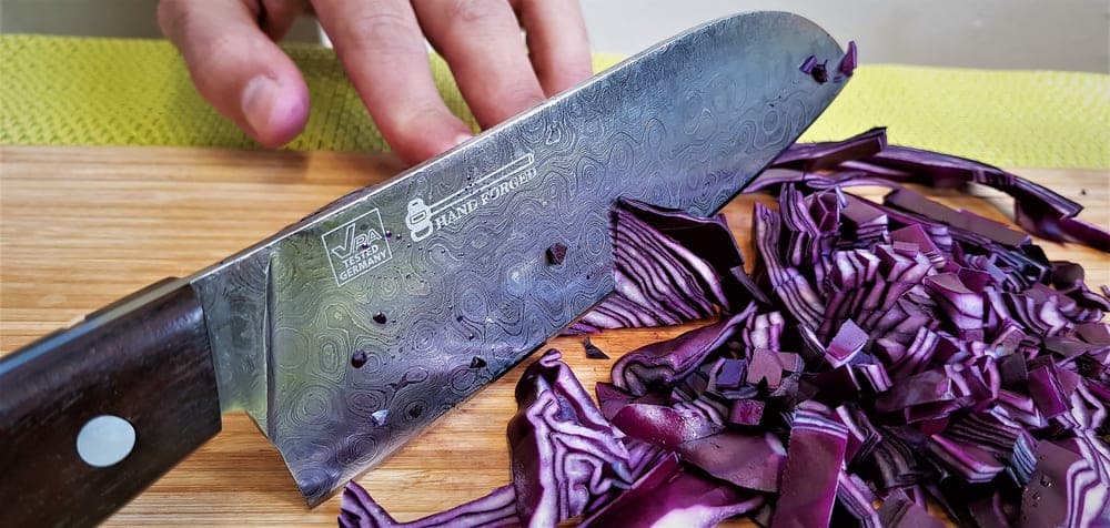 A rectangular-bladed knife slicing through red cabbage