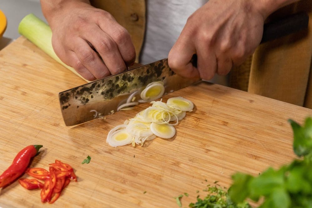 A short flat-profiled kitchen knife slicing onions on a board