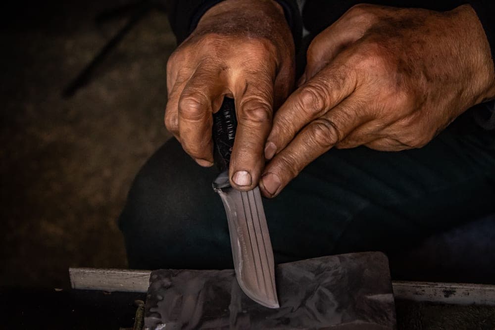 Hands working a knife blade along a sharpening stone